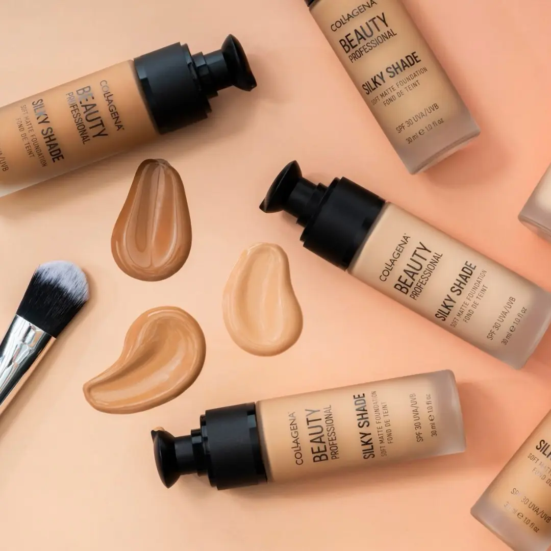 Bottles of Silky Shade Foundation with applied swatches and a brush on a peach background